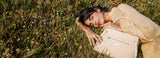 Woman lying in a field of grass with a beige Cavalinho designer handbag next to her