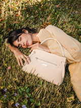Woman lying in a field of grass with a beige Cavalinho designer handbag next to her