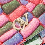 A close-up of a metallic gold LV monogram charm resting on a colorful quilted surface with pink, blue, and green textured panels. #color_pink