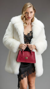 Woman wearing a white fur coat and black lace dress, holding a red burgundy Cavalinho Leather Handbag