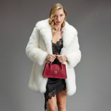 Woman wearing a white fur coat and black lace dress, holding a red burgundy Cavalinho Leather Handbag