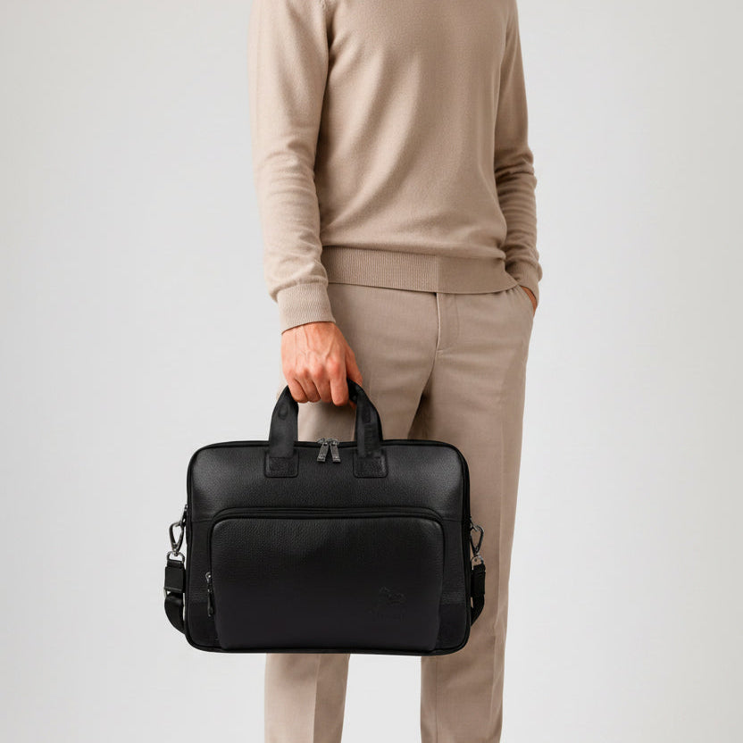 A man in beige clothing holds a black Cavalinho leather laptop briefcase with top handles and a shoulder strap against a light gray studio background SKU 18330608.01 #color_black